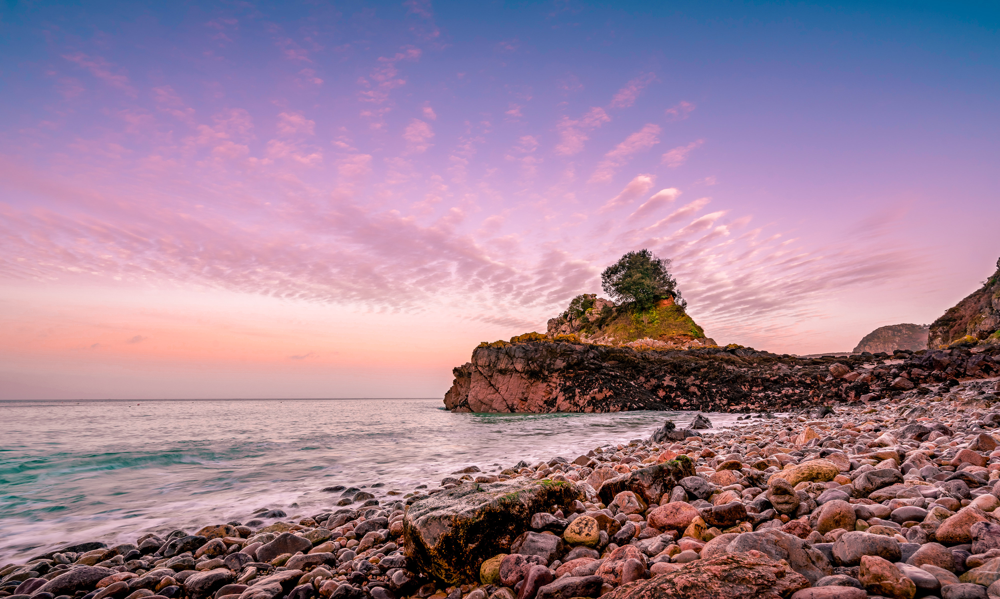 Jersey pebble beach with a sun set and rocks in the distance